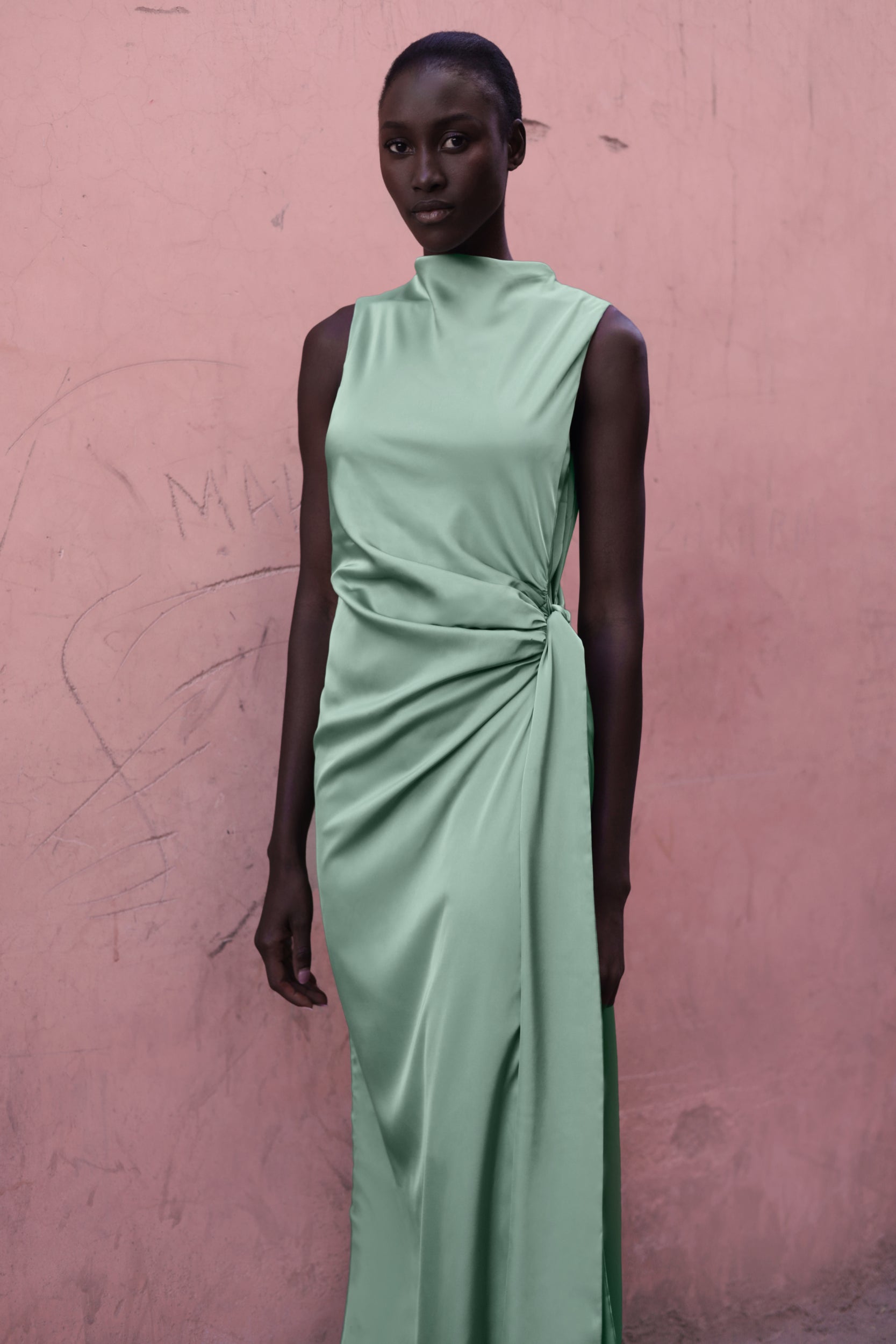 Model wearing the Baobab Vitto Maxi Dress in Jade color posing in front of a pink wall.